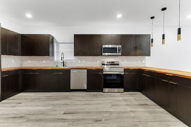 kitchen with hanging light fixtures, dark brown cabinets, appliances with stainless steel finishes, light hardwood / wood-style flooring, and tasteful backsplash