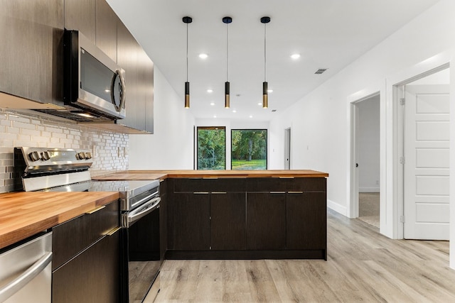 kitchen featuring hanging light fixtures, appliances with stainless steel finishes, butcher block counters, tasteful backsplash, and light wood-type flooring