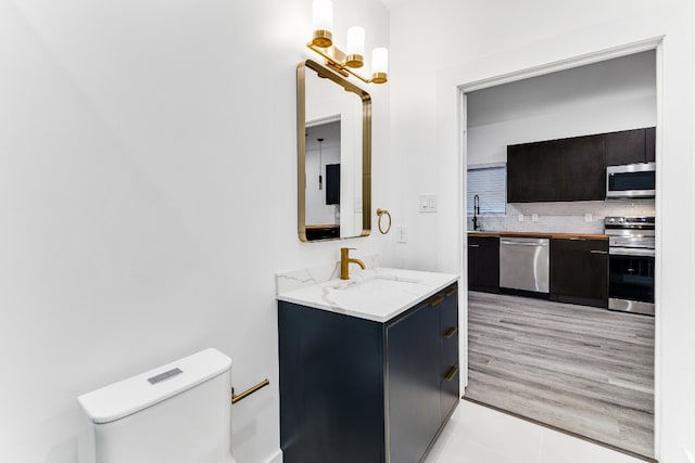 bathroom featuring a chandelier, toilet, large vanity, tasteful backsplash, and tile floors