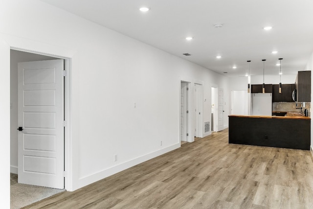 kitchen with white fridge, dark brown cabinetry, tasteful backsplash, light hardwood / wood-style flooring, and pendant lighting