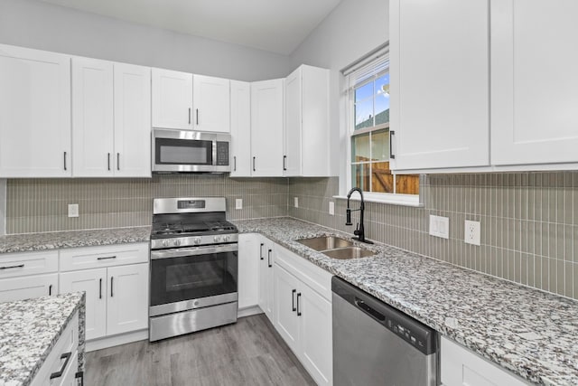 kitchen featuring tasteful backsplash, white cabinets, stainless steel appliances, light hardwood / wood-style flooring, and light stone countertops