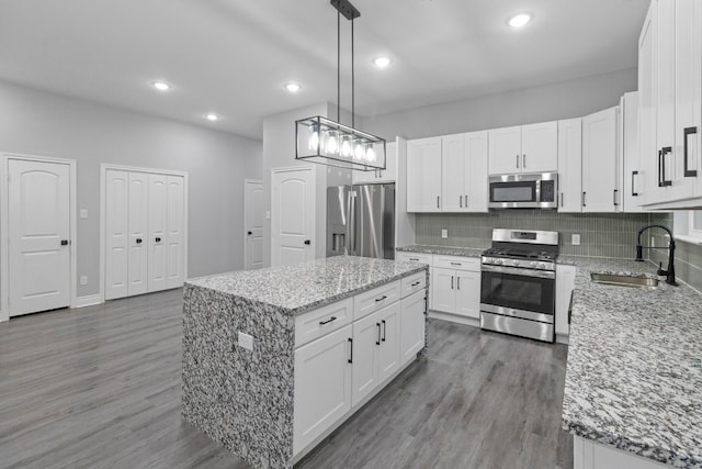 kitchen with appliances with stainless steel finishes, wood-type flooring, backsplash, decorative light fixtures, and sink