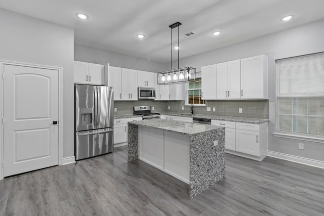 kitchen with dark hardwood / wood-style floors, light stone counters, a kitchen island, hanging light fixtures, and appliances with stainless steel finishes