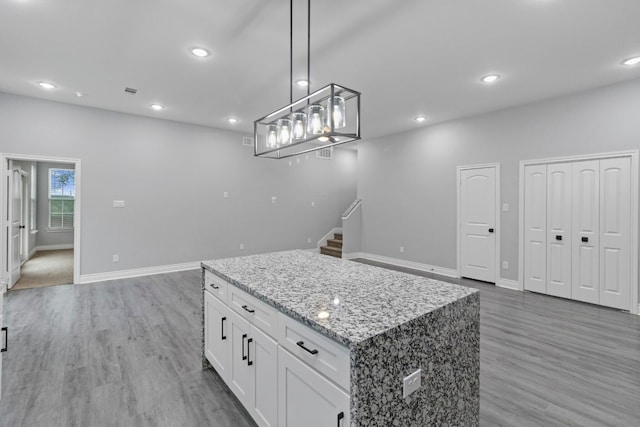 kitchen with pendant lighting, a kitchen island, light stone counters, wood-type flooring, and white cabinetry