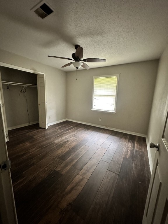 unfurnished bedroom with ceiling fan, a textured ceiling, dark wood-type flooring, and a closet