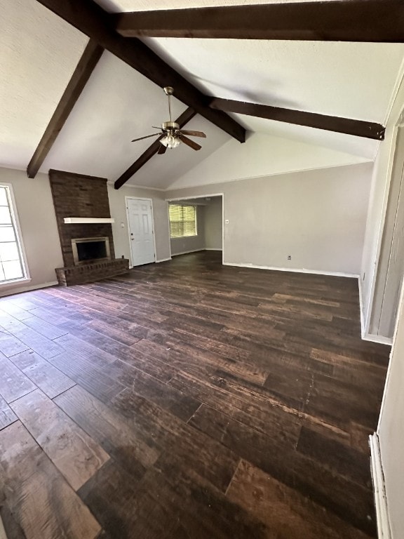 unfurnished living room featuring dark wood-type flooring, vaulted ceiling with beams, brick wall, a fireplace, and ceiling fan