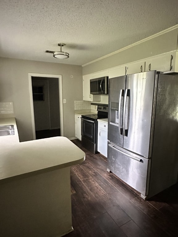 kitchen featuring kitchen peninsula, appliances with stainless steel finishes, backsplash, dark wood-type flooring, and white cabinetry