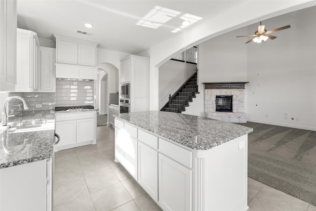 kitchen featuring ceiling fan, a fireplace, light carpet, a center island, and tasteful backsplash