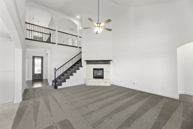 unfurnished living room featuring ceiling fan, a stone fireplace, high vaulted ceiling, and light tile floors