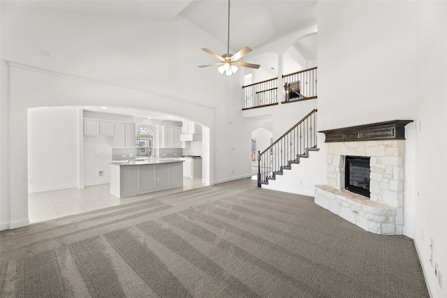 unfurnished living room featuring light carpet, a stone fireplace, ceiling fan, and high vaulted ceiling