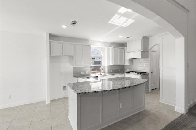 kitchen featuring light tile floors, a center island, dark stone counters, tasteful backsplash, and white cabinets