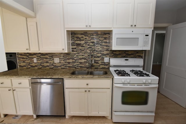 kitchen with dark stone counters, white appliances, washer / dryer, backsplash, and sink