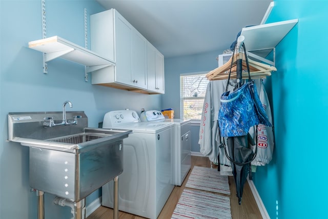 clothes washing area with cabinets, sink, washer and clothes dryer, and light hardwood / wood-style flooring