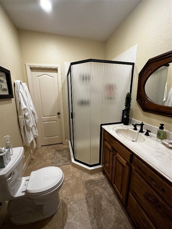 bathroom with a shower with door, vanity with extensive cabinet space, tile flooring, and toilet