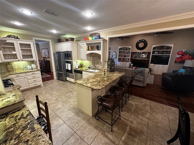 kitchen with backsplash, ornamental molding, stainless steel appliances, and light tile floors