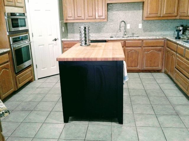 kitchen with tasteful backsplash, butcher block countertops, light tile flooring, and sink