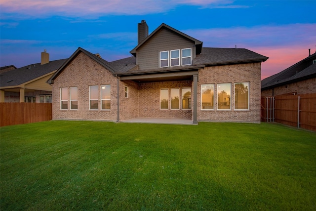 back house at dusk featuring a patio and a yard