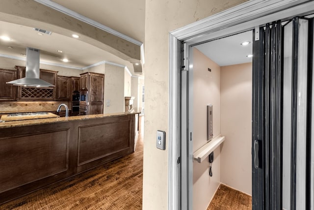 kitchen with backsplash, wall chimney exhaust hood, light stone countertops, and dark wood-type flooring