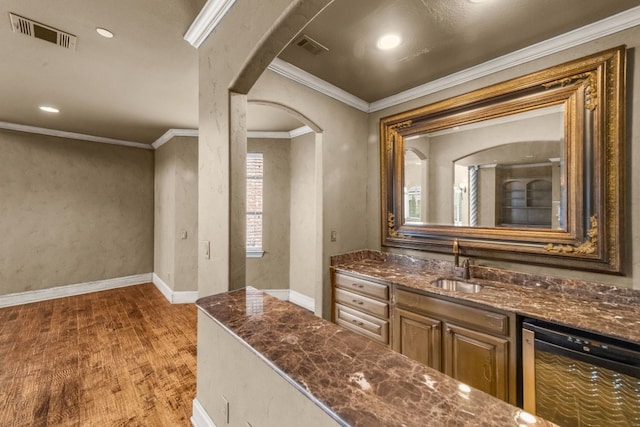 kitchen featuring dishwashing machine, sink, dark stone counters, dark hardwood / wood-style flooring, and ornamental molding