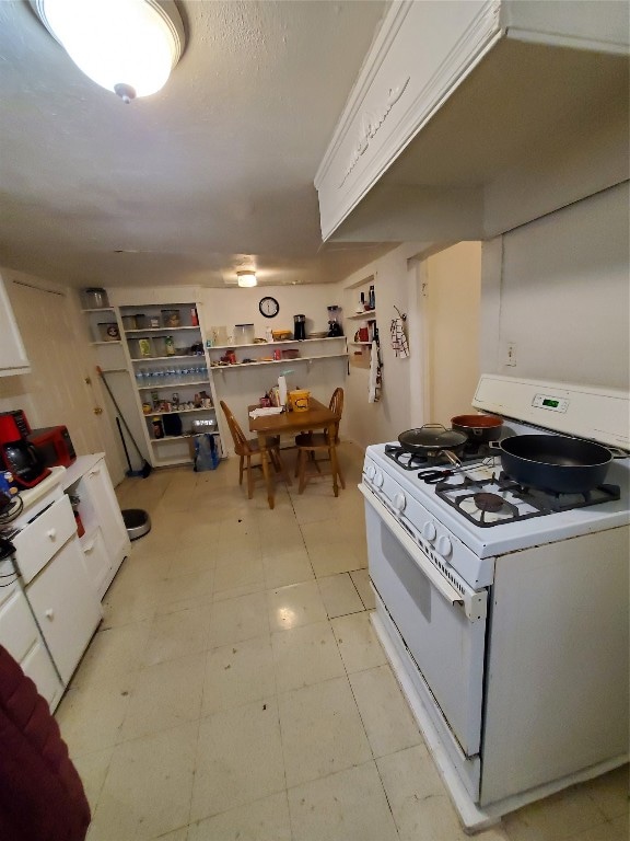 kitchen featuring white range with gas cooktop, light tile floors, and white cabinets