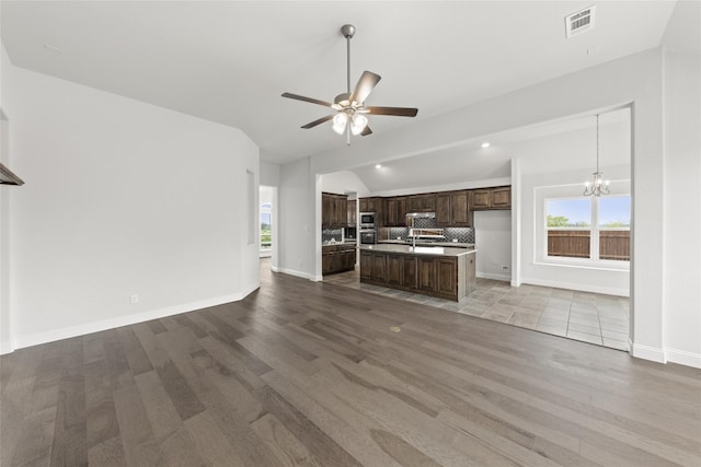 unfurnished living room with light tile floors, sink, ceiling fan with notable chandelier, and vaulted ceiling