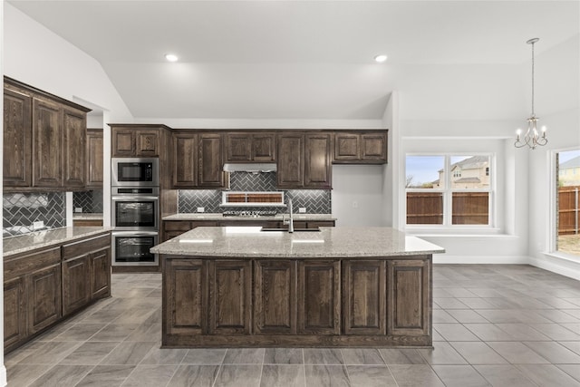 kitchen with a kitchen island with sink, a notable chandelier, light stone counters, and stainless steel appliances