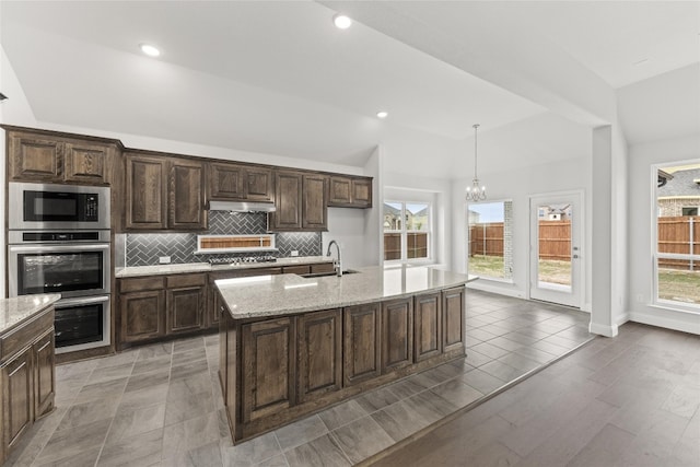 kitchen with dark brown cabinets, appliances with stainless steel finishes, tasteful backsplash, decorative light fixtures, and a notable chandelier