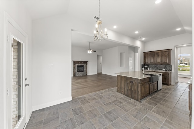 kitchen with tasteful backsplash, a kitchen island with sink, light tile flooring, and lofted ceiling