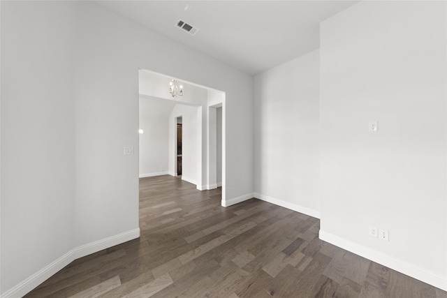 spare room featuring an inviting chandelier and dark wood-type flooring