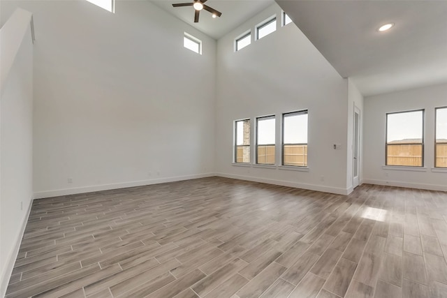 unfurnished living room with a high ceiling, light hardwood / wood-style flooring, plenty of natural light, and ceiling fan