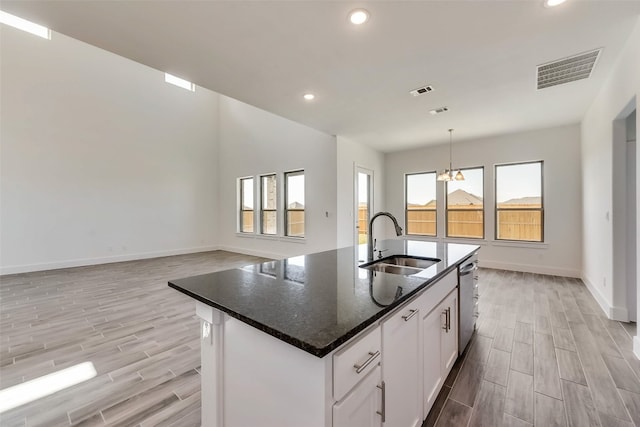 kitchen with white cabinetry, sink, an island with sink, a chandelier, and dark stone counters