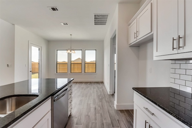 kitchen featuring stainless steel dishwasher, dark stone counters, an inviting chandelier, white cabinetry, and hanging light fixtures