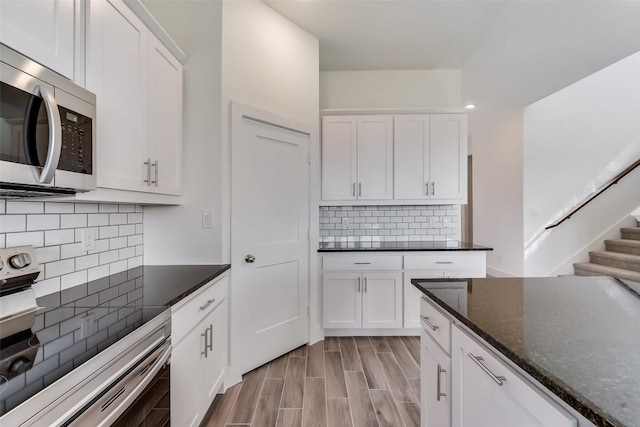 kitchen with decorative backsplash, electric range, white cabinets, and dark stone counters