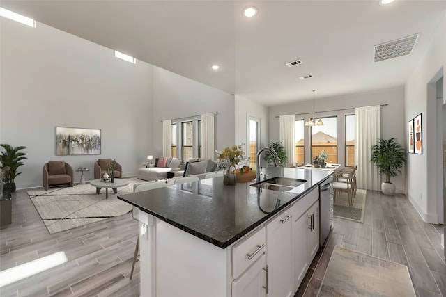 kitchen featuring stainless steel dishwasher, a kitchen island with sink, sink, a notable chandelier, and white cabinetry