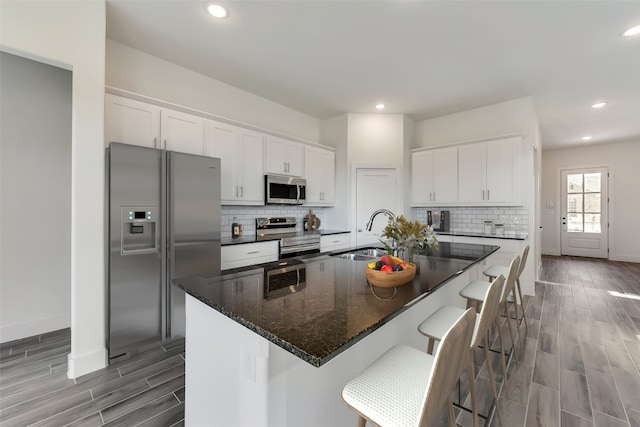 kitchen with a kitchen island with sink, white cabinets, sink, a kitchen bar, and stainless steel appliances