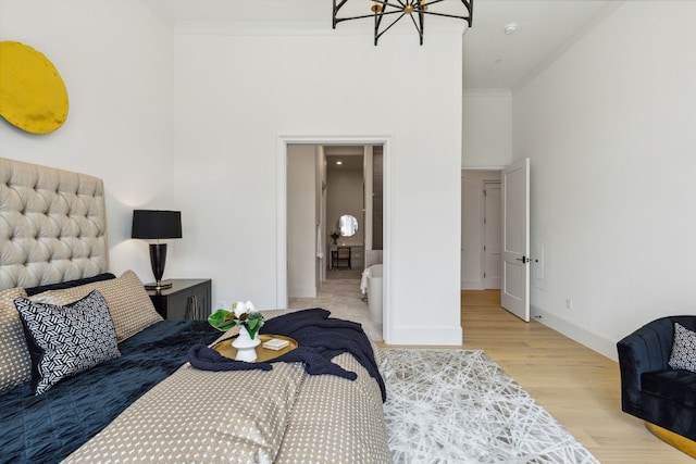 bedroom featuring a notable chandelier, a towering ceiling, crown molding, ensuite bathroom, and light wood-type flooring