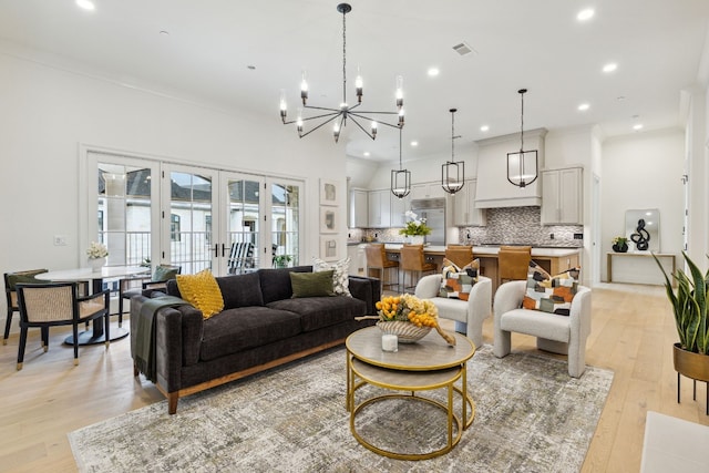 living room featuring an inviting chandelier, ornamental molding, light hardwood / wood-style floors, and french doors