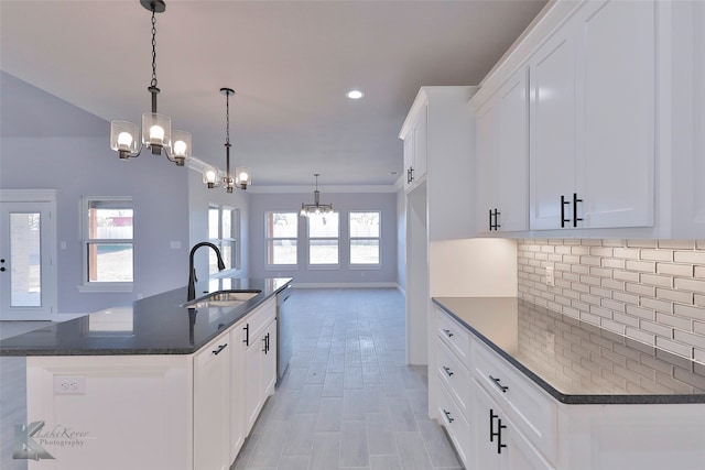 kitchen featuring pendant lighting, an island with sink, sink, white cabinetry, and a notable chandelier