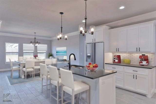 kitchen with pendant lighting, sink, stainless steel refrigerator with ice dispenser, white cabinetry, and a center island with sink