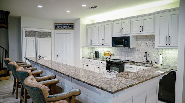 kitchen featuring white cabinets, a kitchen bar, black appliances, and sink