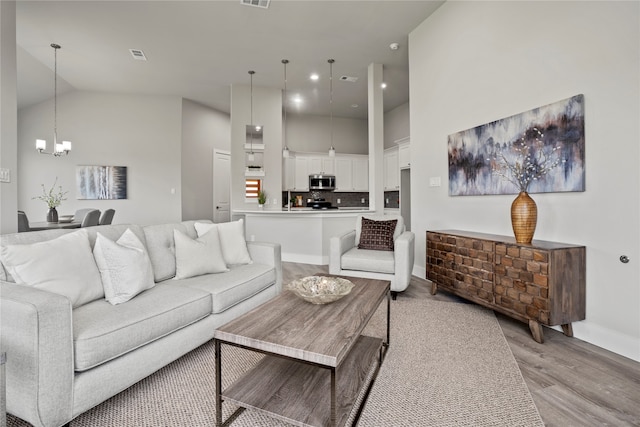 living room featuring light wood-type flooring, high vaulted ceiling, and an inviting chandelier