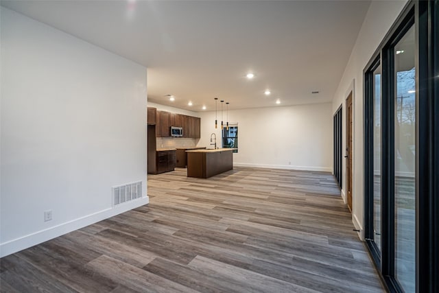 kitchen with wood-type flooring, backsplash, hanging light fixtures, and a kitchen island with sink