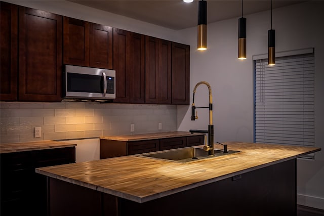 kitchen with a kitchen island with sink, hanging light fixtures, tasteful backsplash, and wooden counters