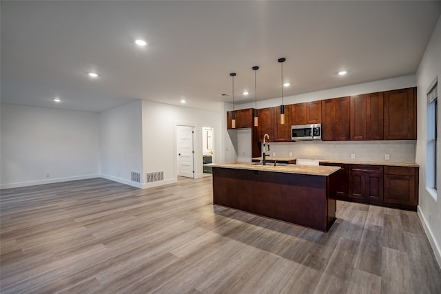 kitchen featuring a kitchen island with sink, pendant lighting, sink, tasteful backsplash, and light wood-type flooring