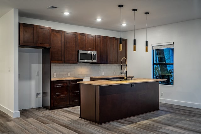 kitchen featuring an island with sink, pendant lighting, hardwood / wood-style floors, backsplash, and sink