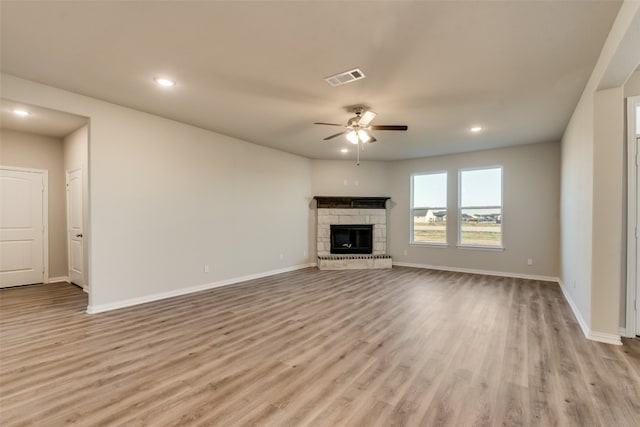 unfurnished living room with ceiling fan, light hardwood / wood-style floors, and a stone fireplace