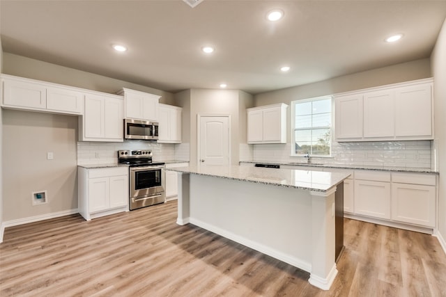 kitchen featuring white cabinets, stainless steel appliances, light wood-type flooring, and light stone counters