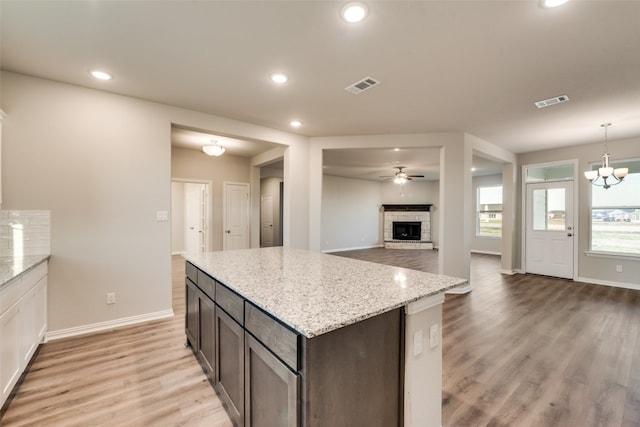 kitchen with light stone counters, light hardwood / wood-style floors, dark brown cabinets, ceiling fan with notable chandelier, and hanging light fixtures