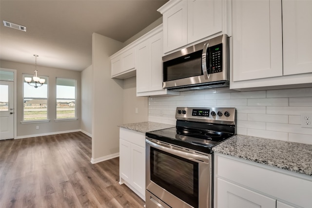 kitchen with an inviting chandelier, appliances with stainless steel finishes, light stone countertops, and white cabinets