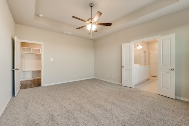 unfurnished bedroom with ceiling fan, a spacious closet, light carpet, and a closet